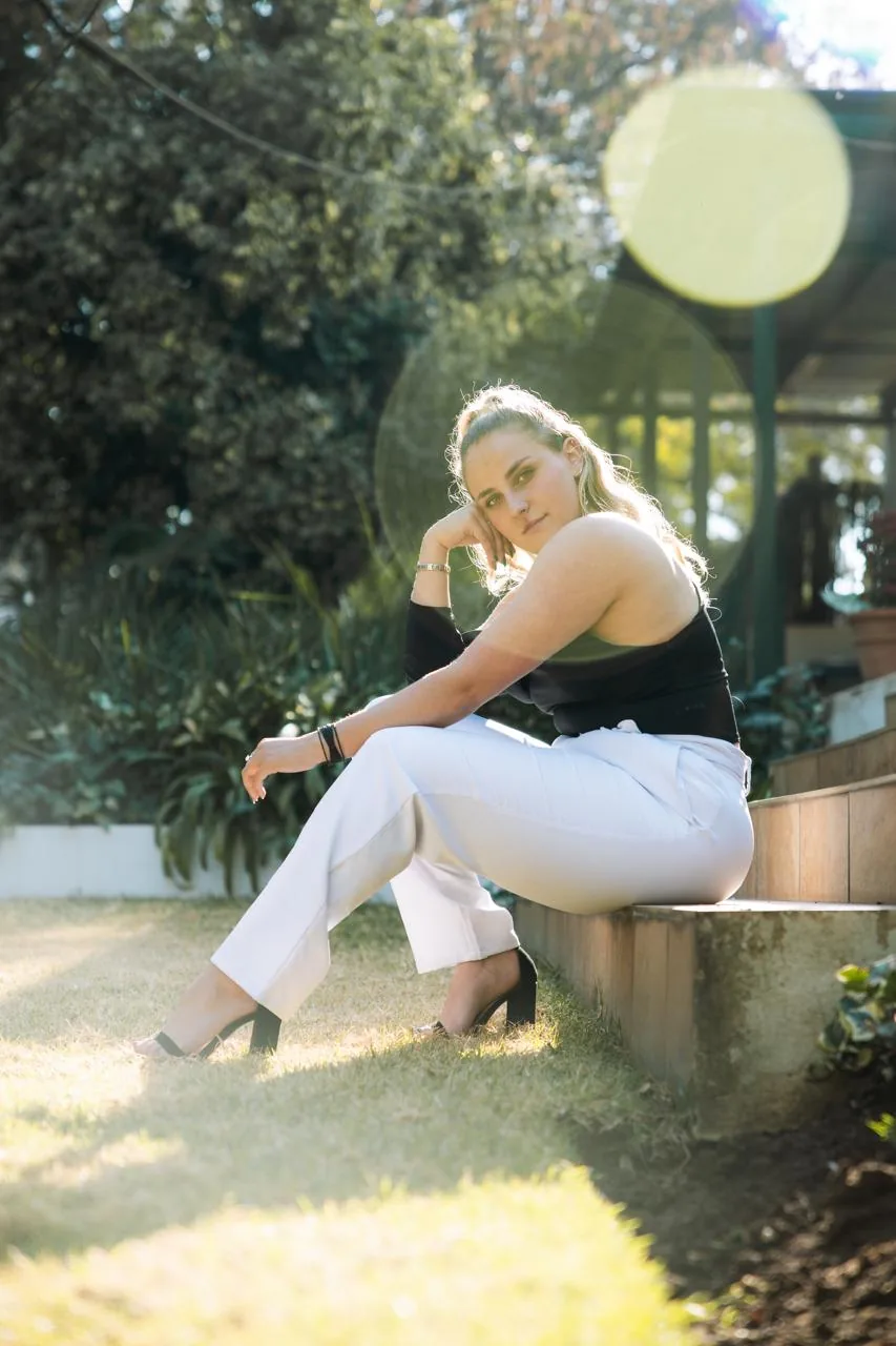 Dani T sitting on a low wall in a garden in the afternoon sun